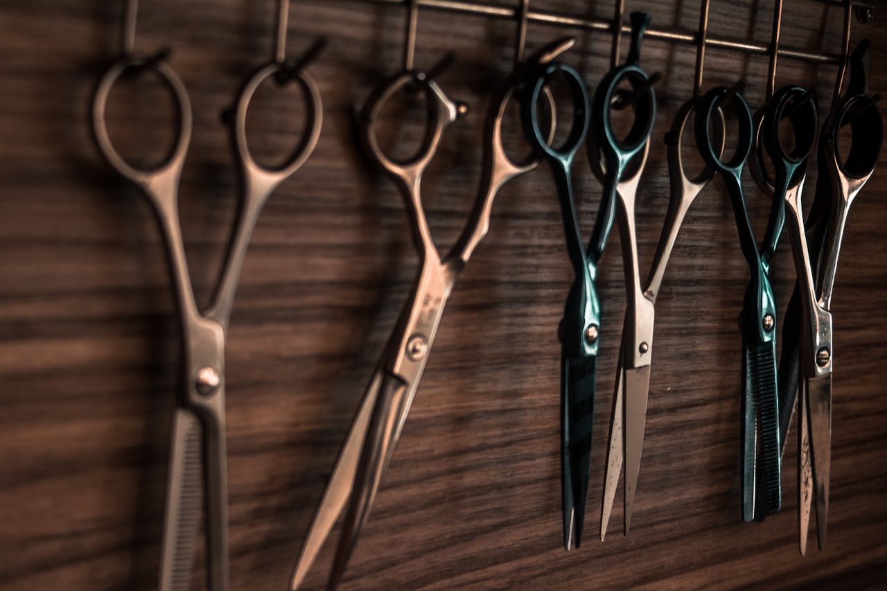 Home A collection of vintage barber scissors hanging on a wooden wall, showcasing sharp tools for hair cutting.