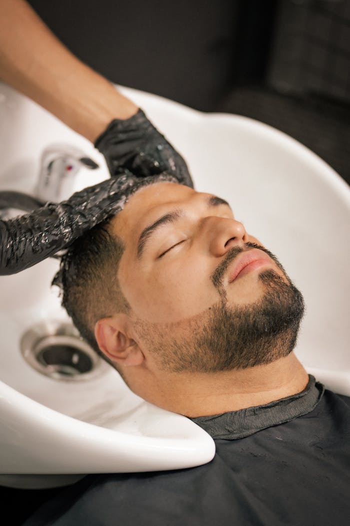 Home A man with closed eyes enjoys a calming hair wash at a barbershop sink.