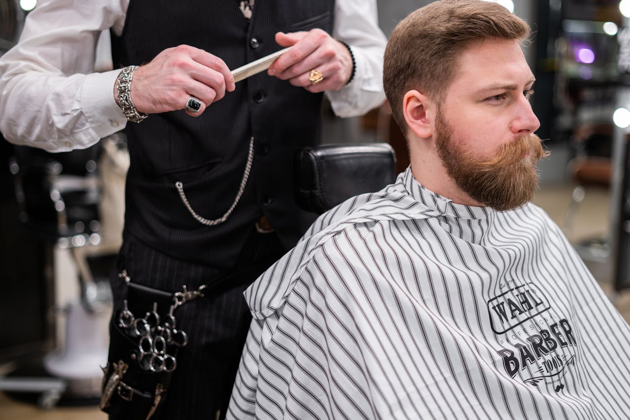 Home A barber meticulously grooming a bearded man in a stylish barbershop setting, showcasing modern men
